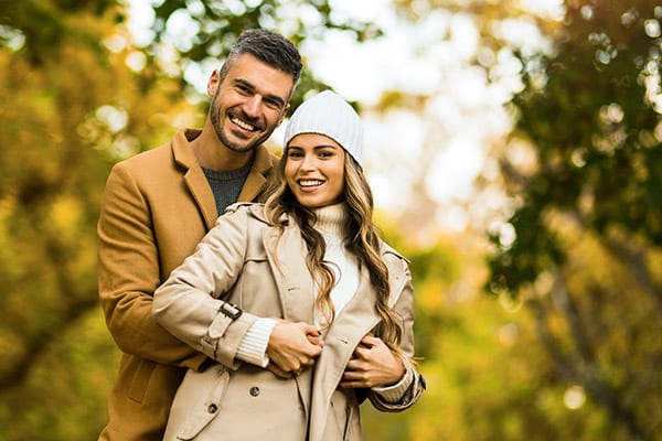 Candid young couple embracing while enjoying a walk together in autumn nature. They are looking at camera.